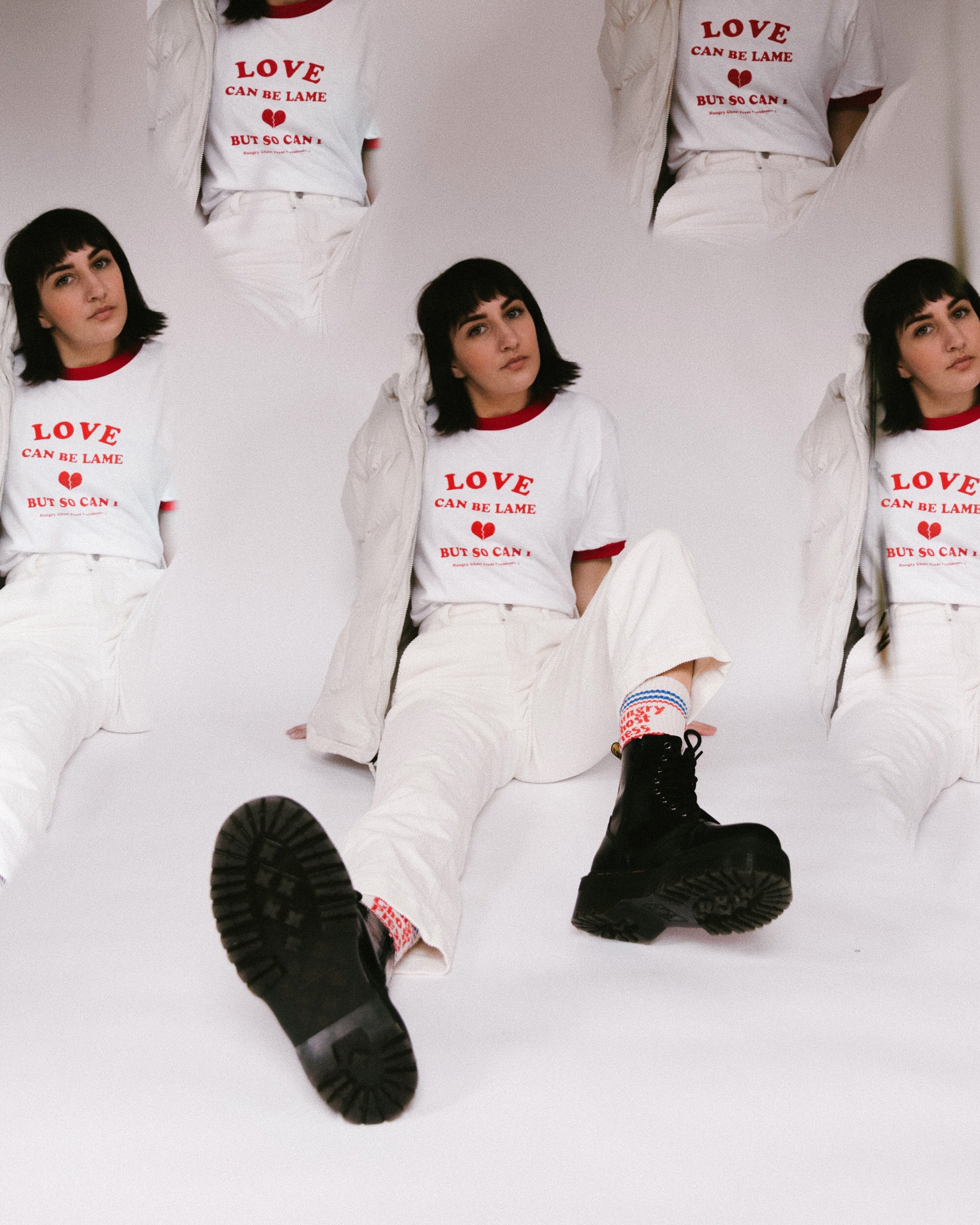 Person wearing a white outfit with 'LOVE CAN BE LAME' text, sitting on a white background while wearing the New England Hungry Ghost Press Socks.